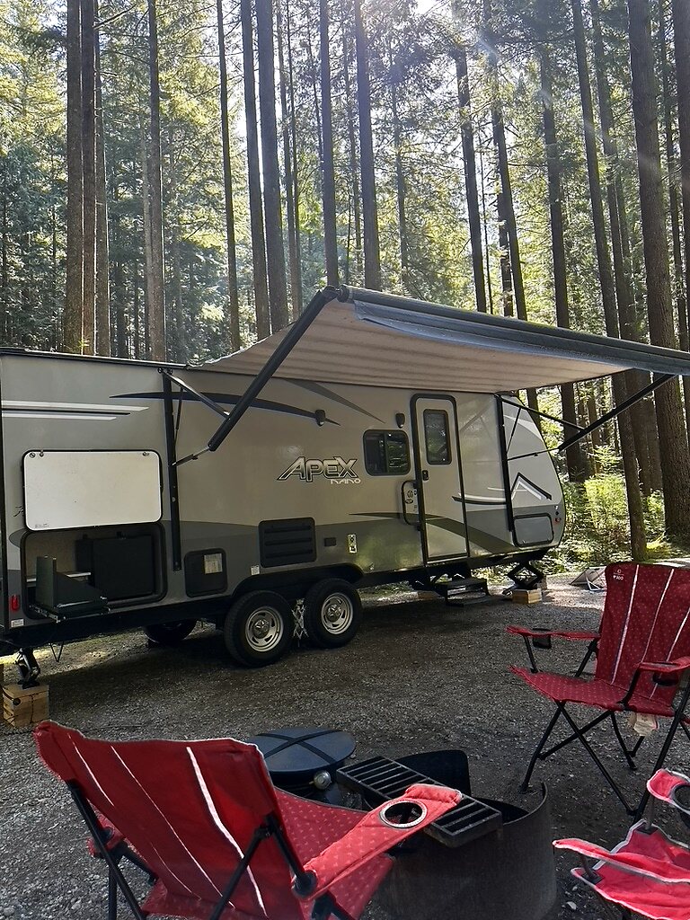 Our camper set up in a British Columbia forest with the awning out and chairs ready
